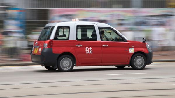 A red and white high-tech taxi equipped with advanced driver monitoring systems and electronic payment technology speeds along a city street.