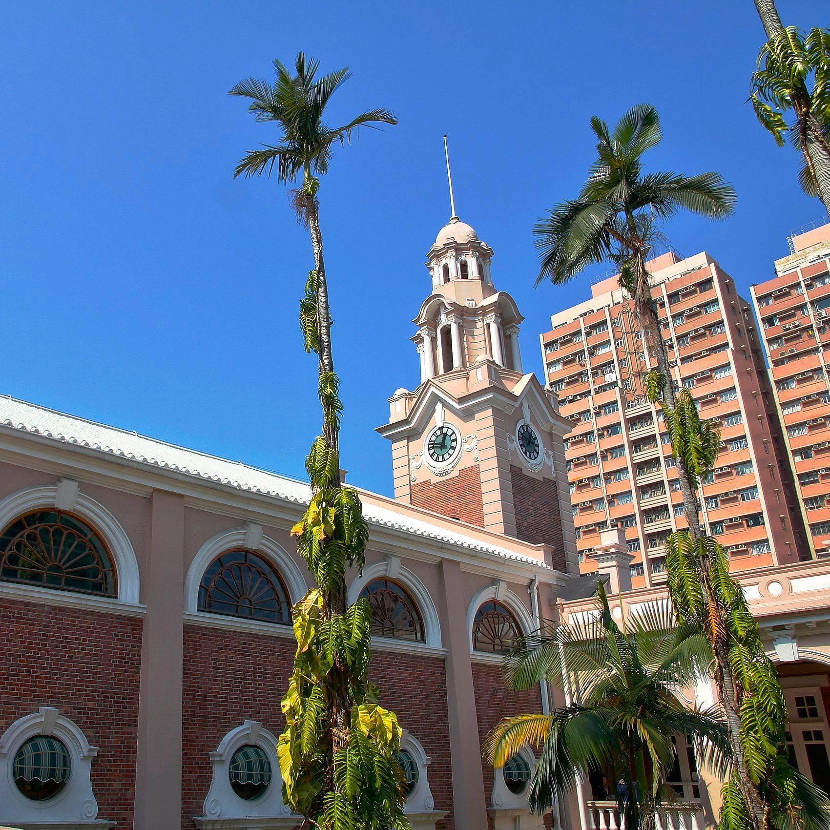 A tall clock tower and a pink building with many windows in Hong Kong.