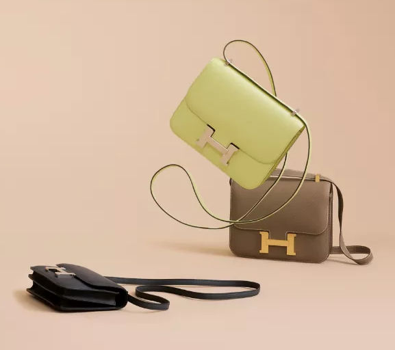 a photo of three hermes constance bags in lime green, beige, and black