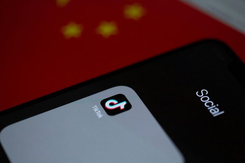 a photo of a phone displaying the tiktok app on a chinese flag, used in an article on the latest tiktok ban in america